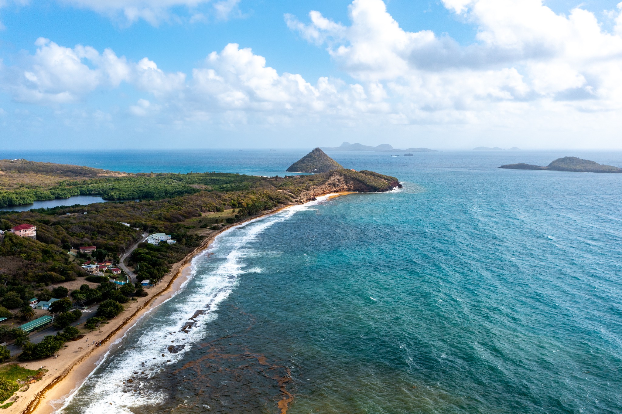 Aerial view of a green headland meeting turquoise water beneath a cloud-filled sky