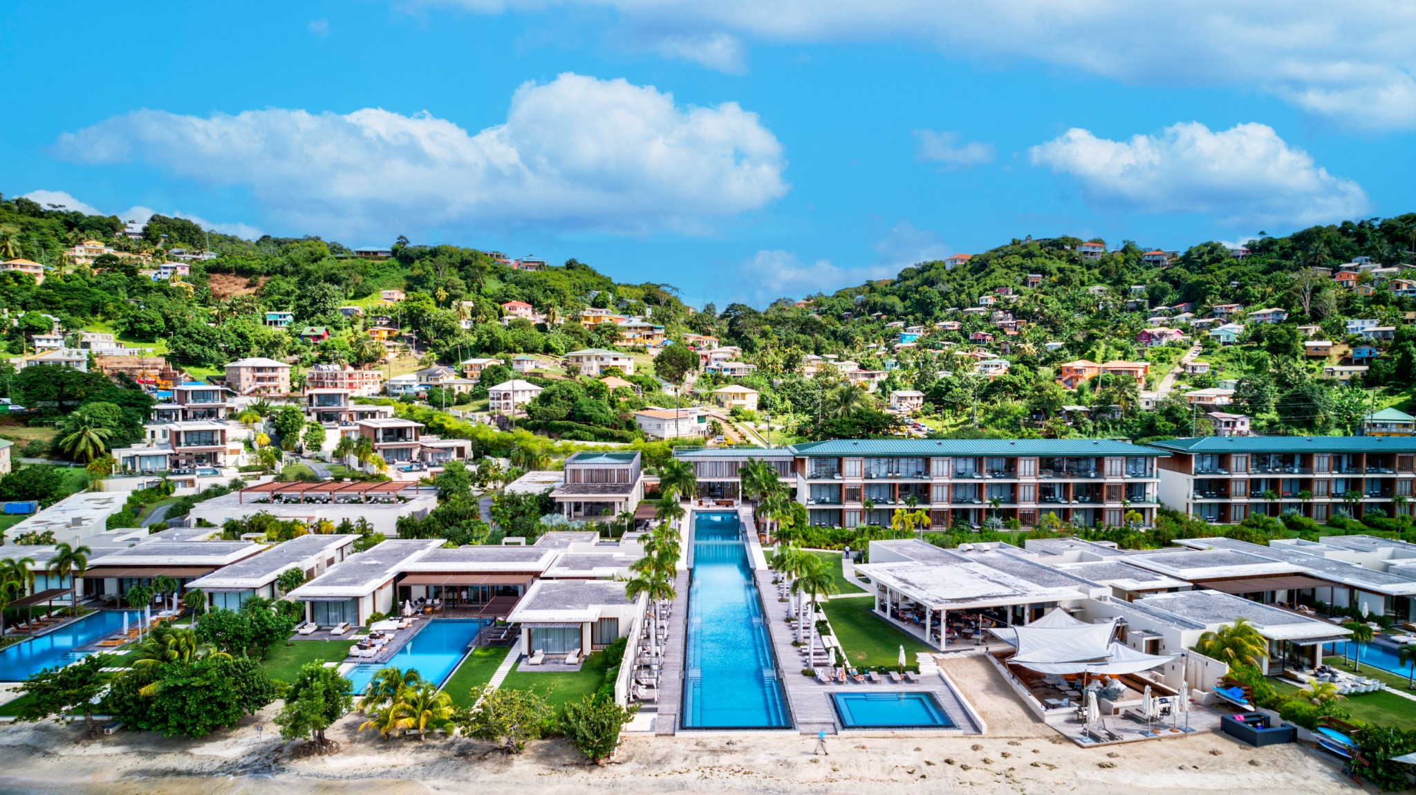 Aerial view of a terraced hillside resort with long pools running down to a beach
