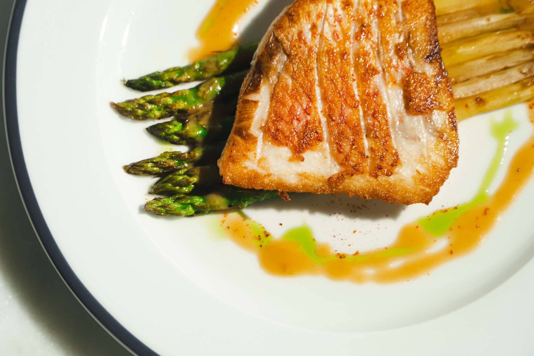Seared fish fillet with asparagus and herb oil plated on white porcelain