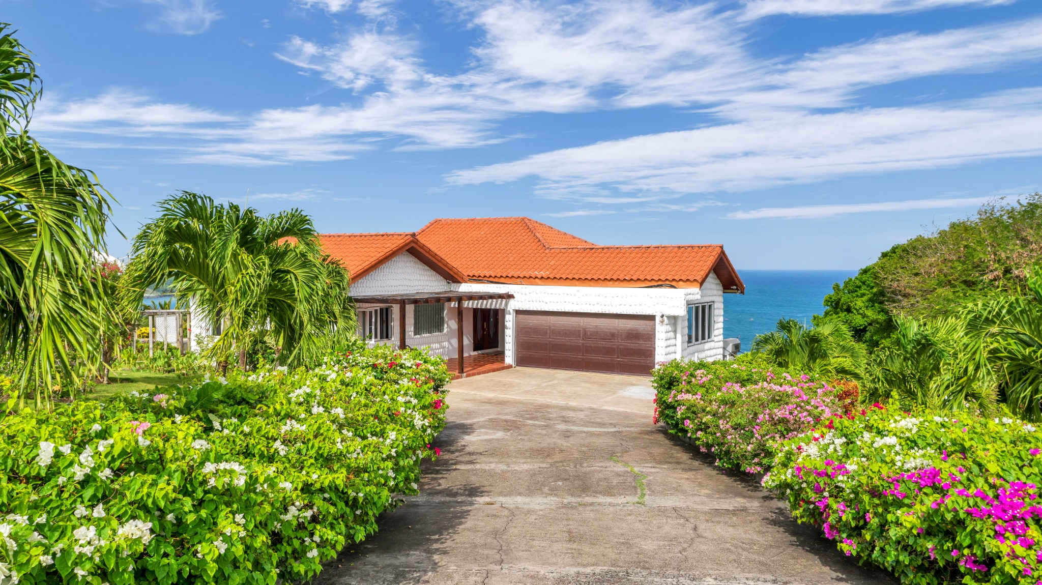 Red-roofed villa approached through a flowering tropical garden with sea views
